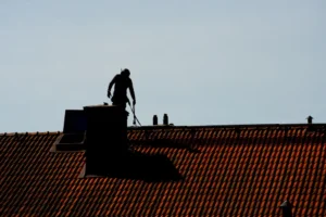 Chimney sweep performing chimney sweep service on a tiled roof.