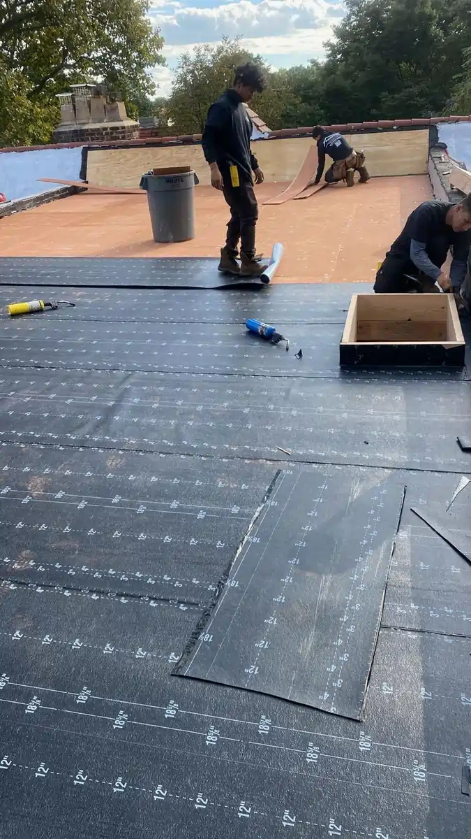 Roofers installing underlayment on a flat roof as part of budget roof options for residential buildings.