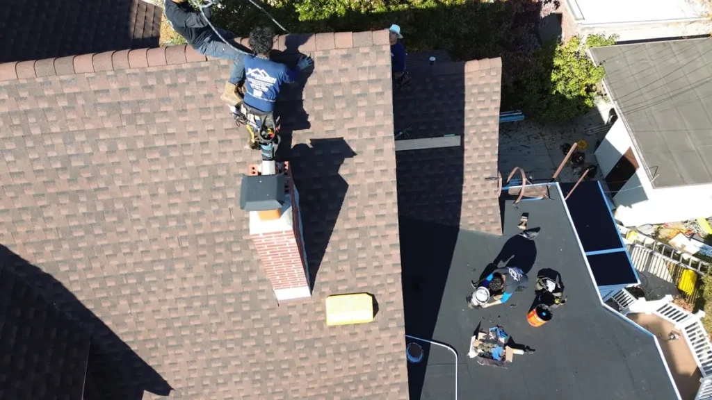 Roofer installing chimney flashing on asphalt shingles, one of the cheapest roof materials, on a residential home.