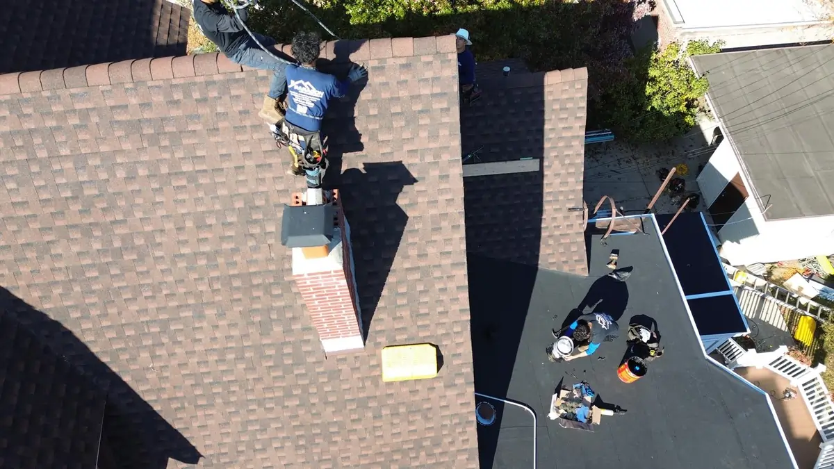 Roofer installing chimney flashing on asphalt shingles, one of the cheapest roof materials, on a residential home.
