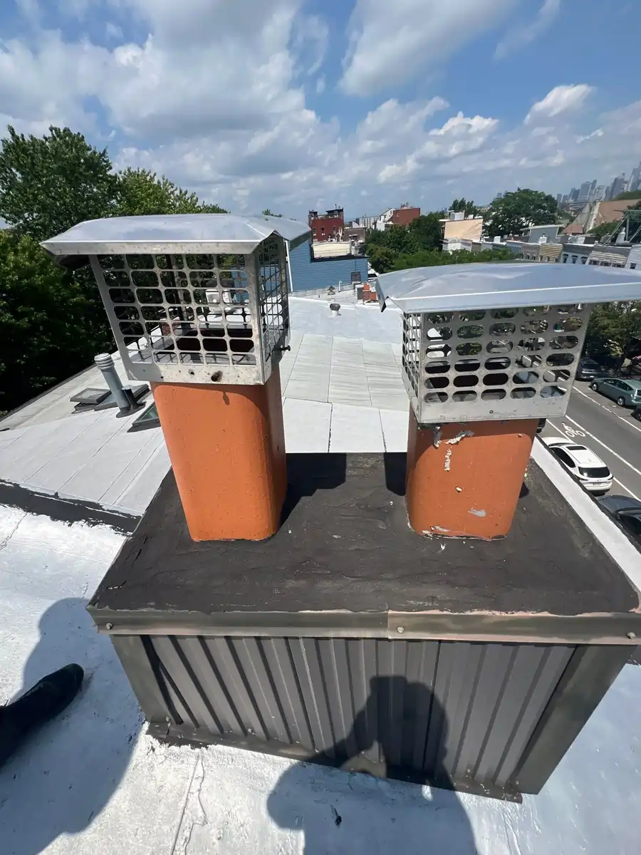 Old chimney ventilation system featuring dual flue caps on a flat rooftop, designed to improve airflow and maintain safety in older buildings.